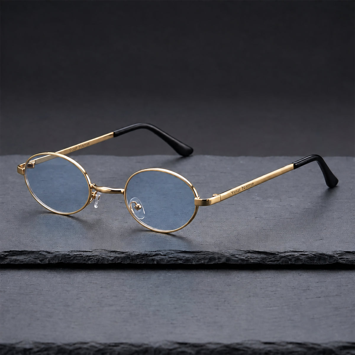Gold-tone oval sunglasses with pale blue lenses and black temple tips, viewed at an angle on dark slate.