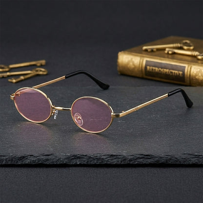 ROSHFORT gold oval sunglasses resting on dark slate beside a book