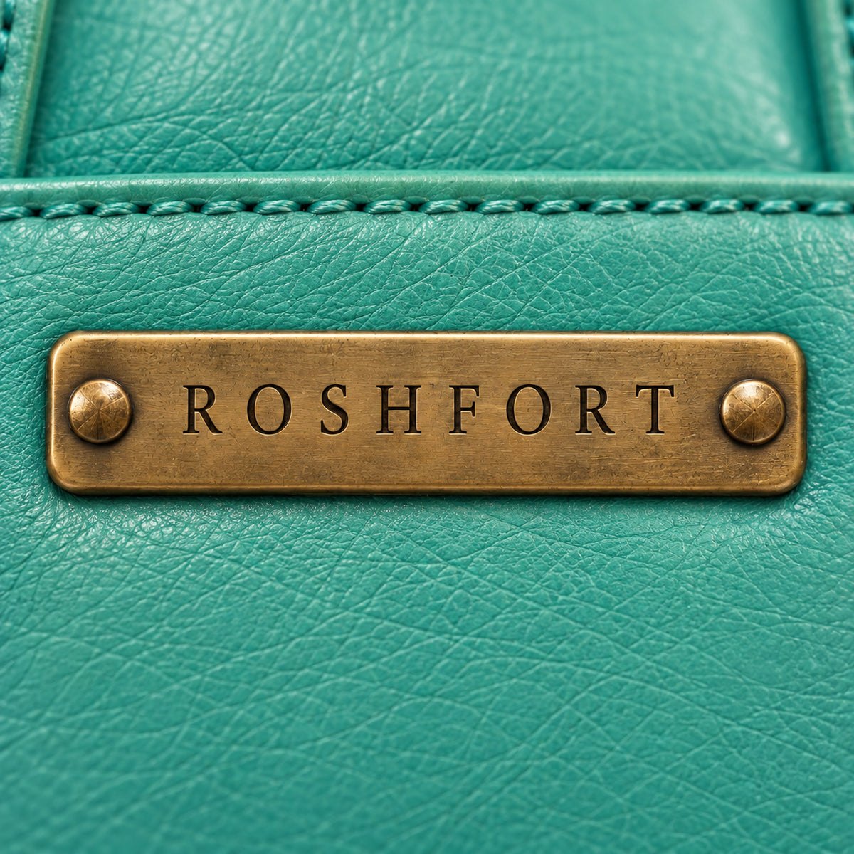 Close-up of the aged brass ROSHFORT name plate on the teal leather