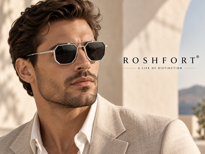 Man in a light jacket wearing silver octagonal sunglasses outdoors.